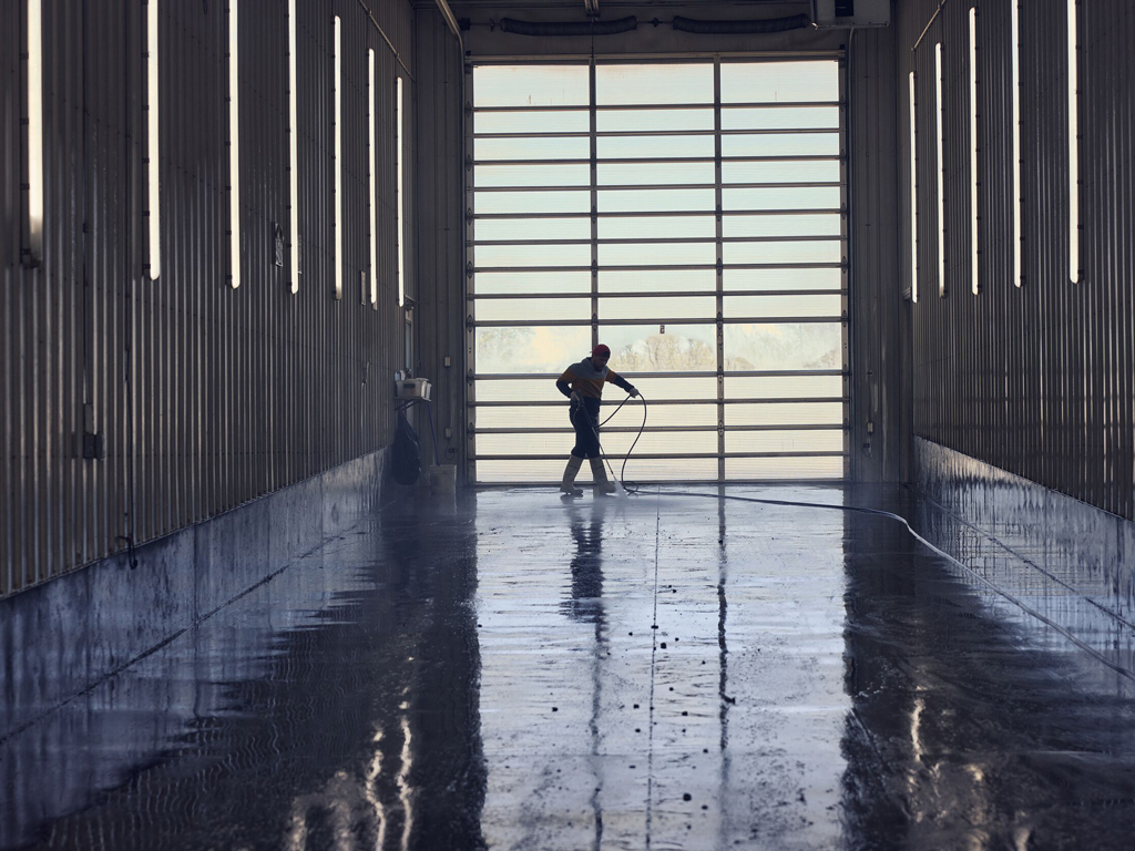 Worker washing out the truck bay for biosecurity