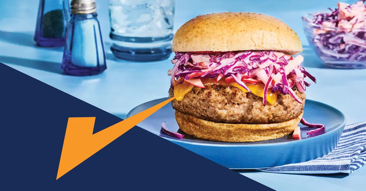 A close-up of a juicy, grilled ground pork burger on a toasted bun, topped with fresh lettuce, tomato, and cheese.